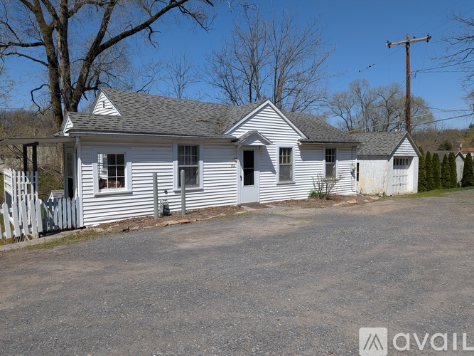 A white house with a grey roof and a sign that says "available" in the front yard.