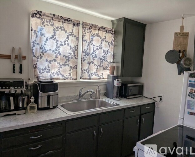 A kitchen with a sink, a window with curtains, and a fridge.