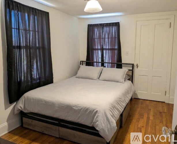 A bedroom with a bed, wooden floors, and a window with curtains.