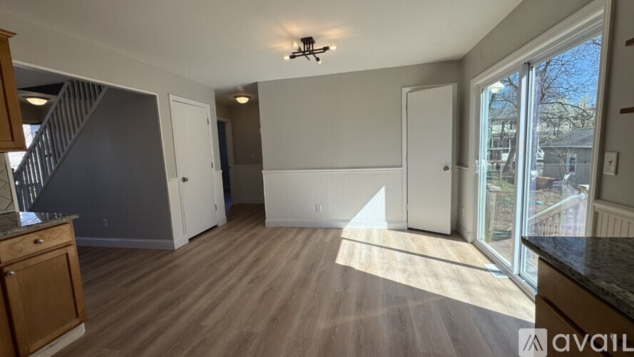A spacious room with wooden flooring and a staircase on the left side.