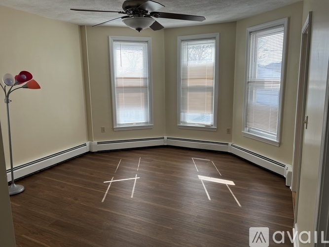 A room with a fan, two windows, and a floor marked with white lines.