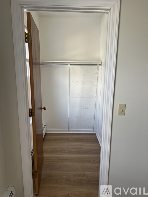 A white door with a gold handle is open to a room with a white wall and a wooden floor.