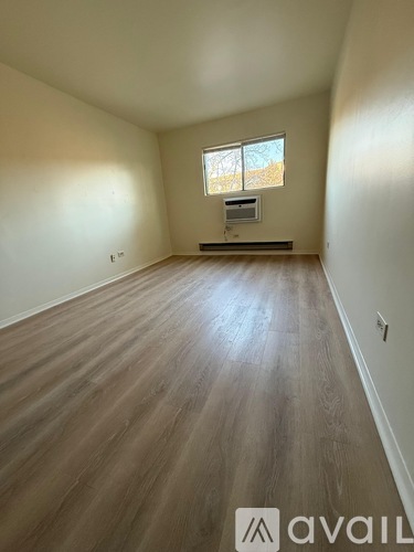 A room with wooden flooring and a window with a view of trees outside.