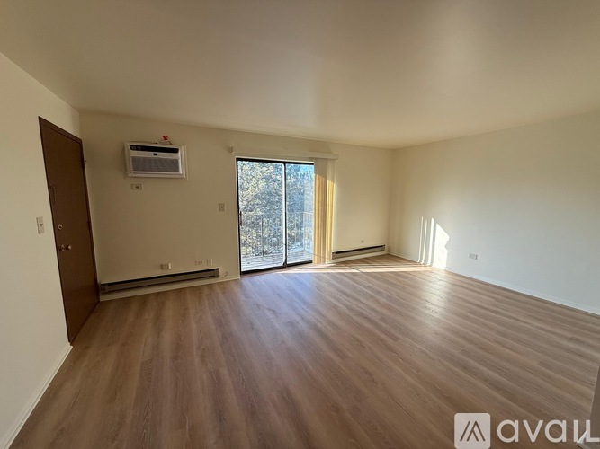 A spacious room with wooden flooring and a sliding glass door leading to a balcony.