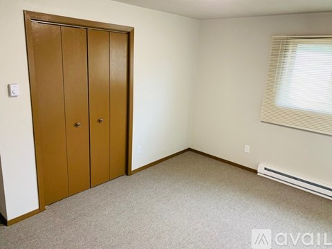 A bedroom with a brown wardrobe and a window with blinds.