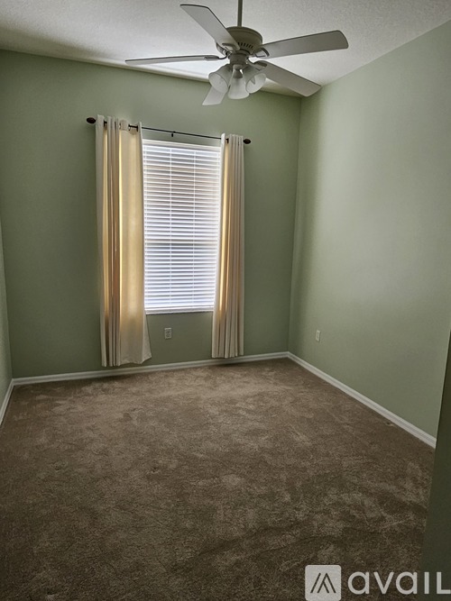 A room with a carpeted floor, a ceiling fan, and a window with curtains.