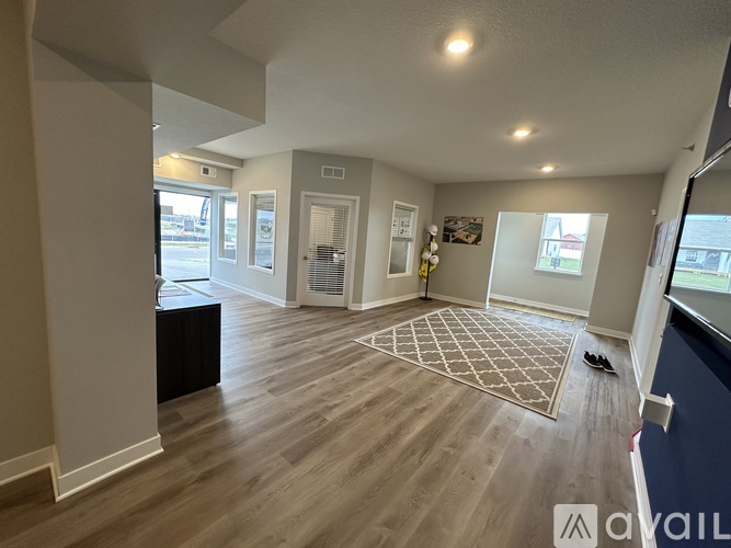 A spacious room with wooden flooring and a large rug in the center.