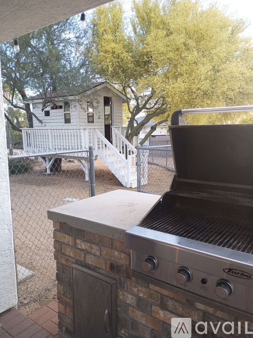 A BBQ grill is in the foreground of a backyard with a house and tree in the background.