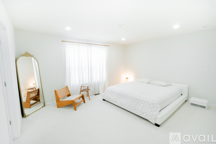 A white bedroom with a large bed, a chair, and a mirror.