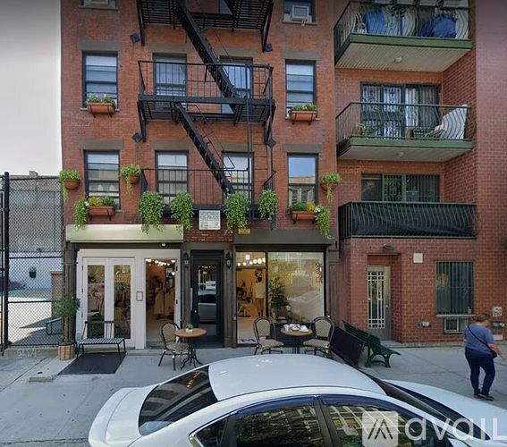 A white car is parked in front of a building with a black metal fence.