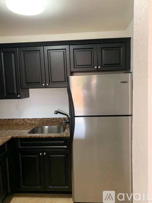A kitchen with black cabinets and a stainless steel refrigerator.