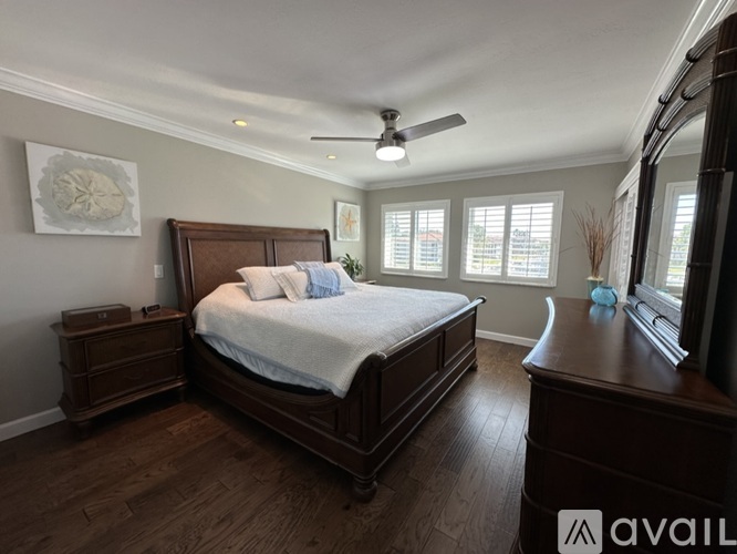 A bedroom with a large bed, wooden dresser, and a ceiling fan.