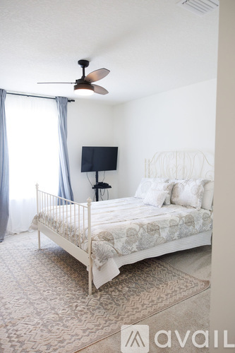 A bedroom with a bed, fan, and window with curtains.
