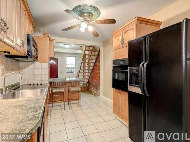 A kitchen with a black refrigerator, a ceiling fan, and a staircase in the background.