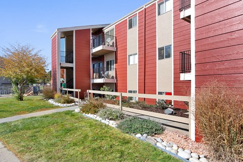 A red and beige apartment building with a white fence and green grass in front.