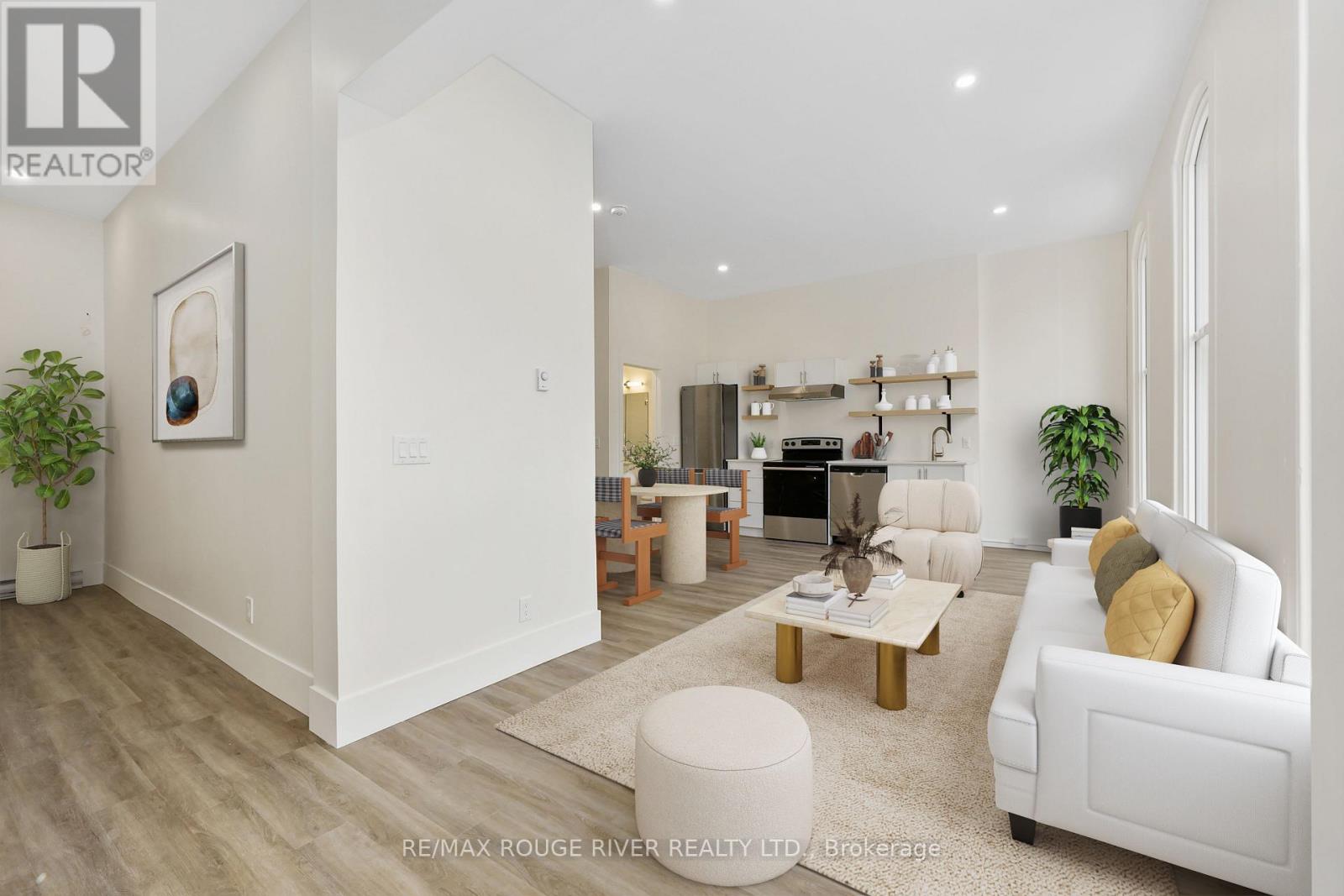 A well-lit, spacious living room with a white sofa, wooden coffee table, and a large painting on the wall.