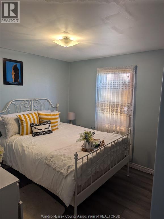 A bedroom with a white bed and a painting of a woman on the wall.