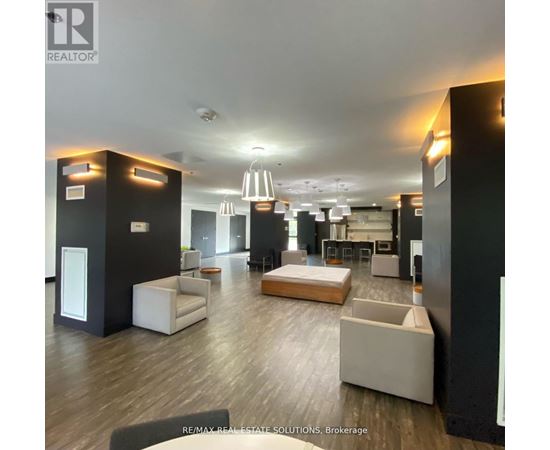 A spacious living room with a white sofa set and a kitchen area in the background.