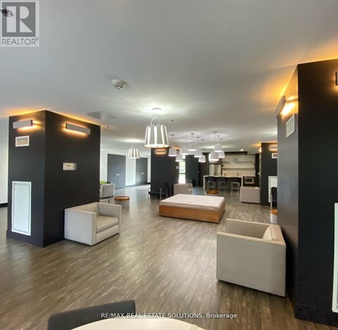 A spacious living room with a white sofa set and a kitchen area in the background.