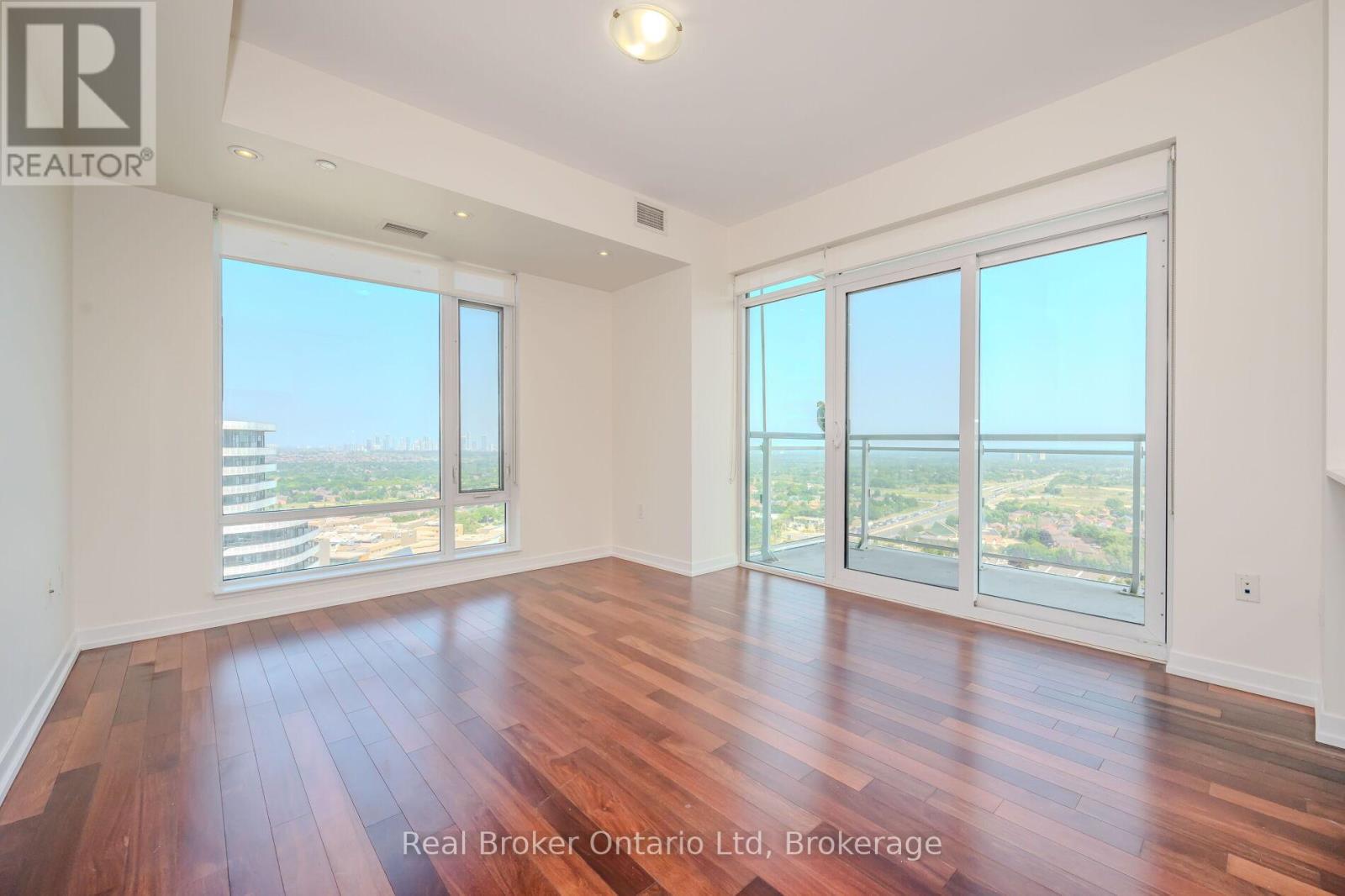 A spacious room with wooden floors and large windows overlooking a cityscape.