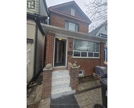 A house with a brown brick facade and a black trash bin in front.