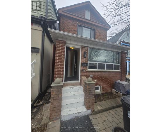 A house with a brown brick facade and a black trash bin in front.
