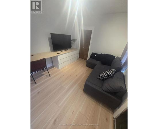 A living room with a grey couch and a television on a white desk.