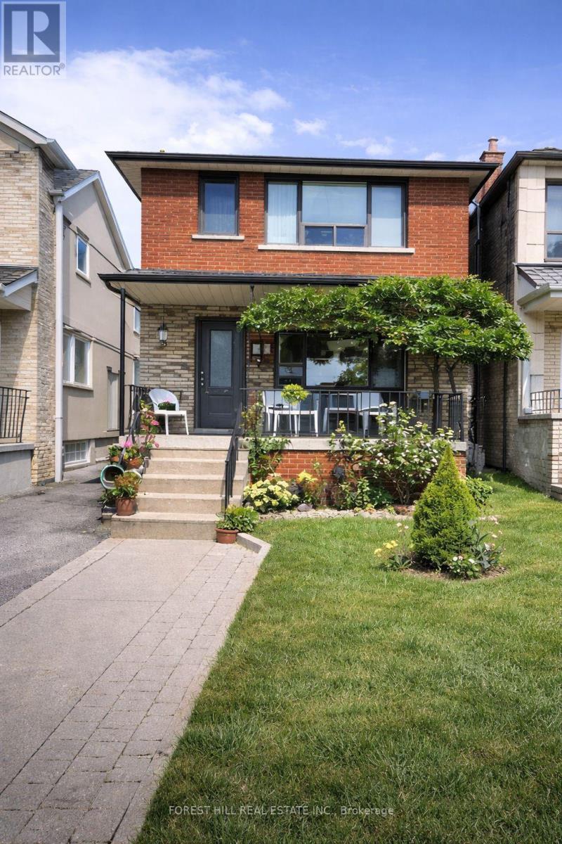 A house with a red brick facade and a black door is surrounded by a well-kept lawn and a paved walkway.