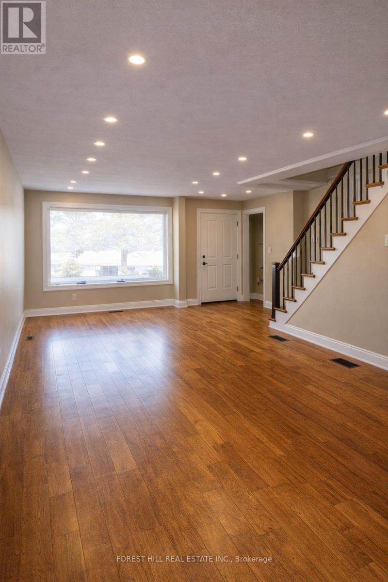 A spacious room with wooden floors and a staircase.
