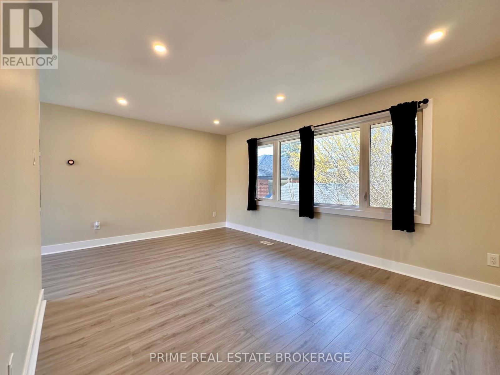 A spacious room with wooden flooring and a large window with black curtains.