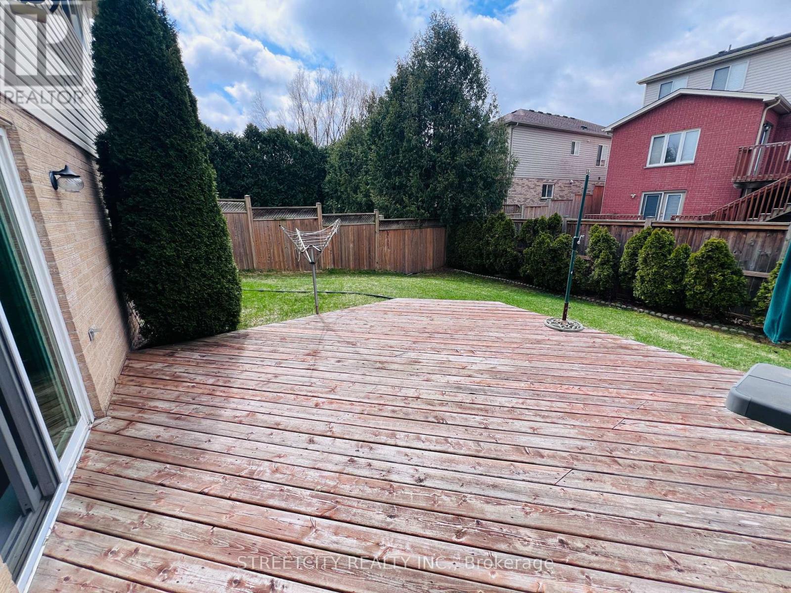 A wooden deck in a backyard with a fence and trees in the background.