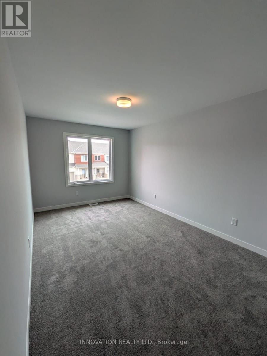 A room with grey carpet and a window showing a building outside.