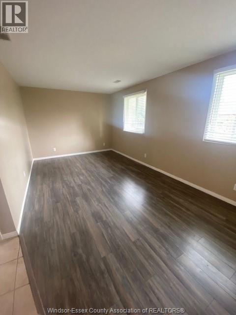 A room with wooden flooring and two windows.