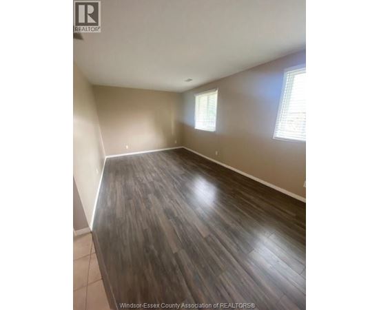 A room with wooden flooring and two windows.