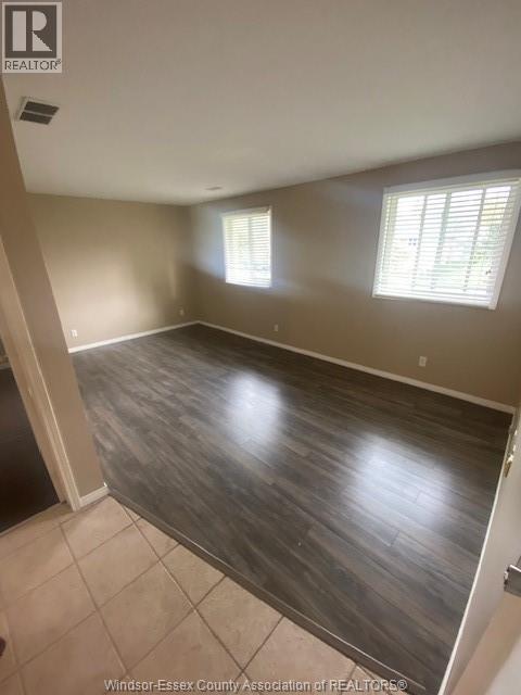A room with wooden flooring and two windows.