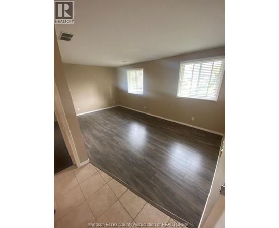 A room with wooden flooring and two windows.