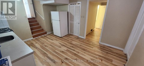 A kitchen area with a refrigerator and stairs leading to another room.