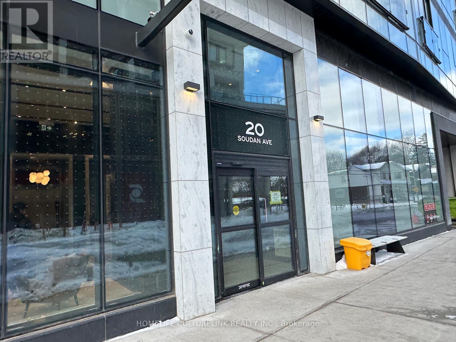 The image shows the exterior of a building with a glass door and a sign that reads "20 SOUDAN AVE".