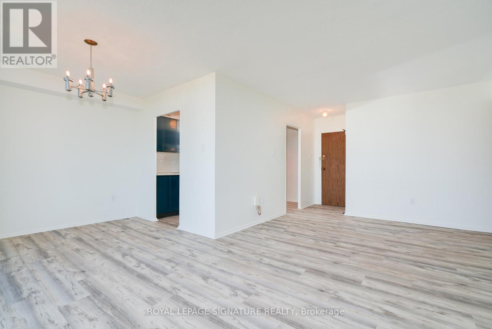 A white room with a chandelier and wood flooring.