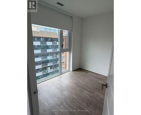 A room with a sliding glass door leading to a balcony with a view of a building.