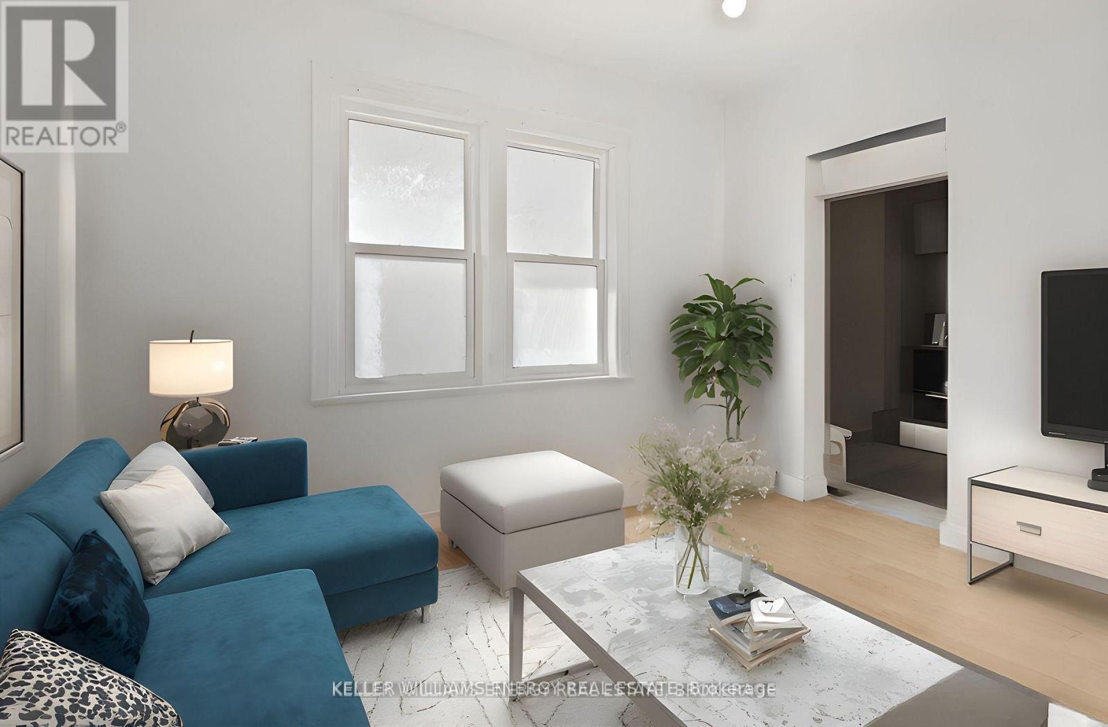 A living room with a blue couch, a white ottoman, a glass coffee table, and a flat-screen TV.