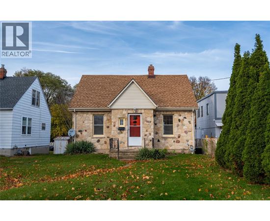 A small house with a red door is surrounded by a grassy area with fallen leaves.