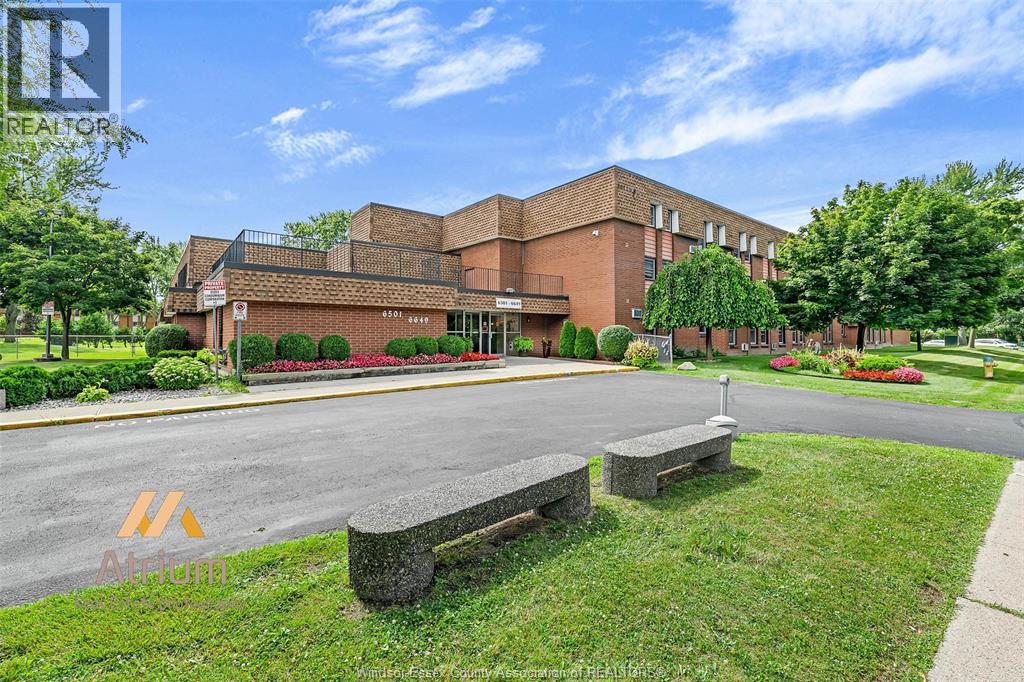 A building with a red brick facade is surrounded by greenery and a clear blue sky.