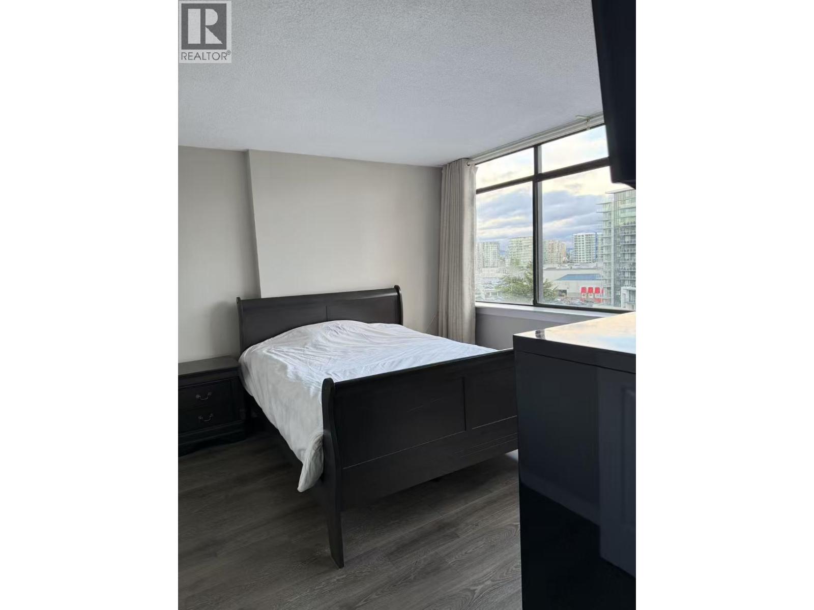 A bedroom with a bed, nightstand, and window.