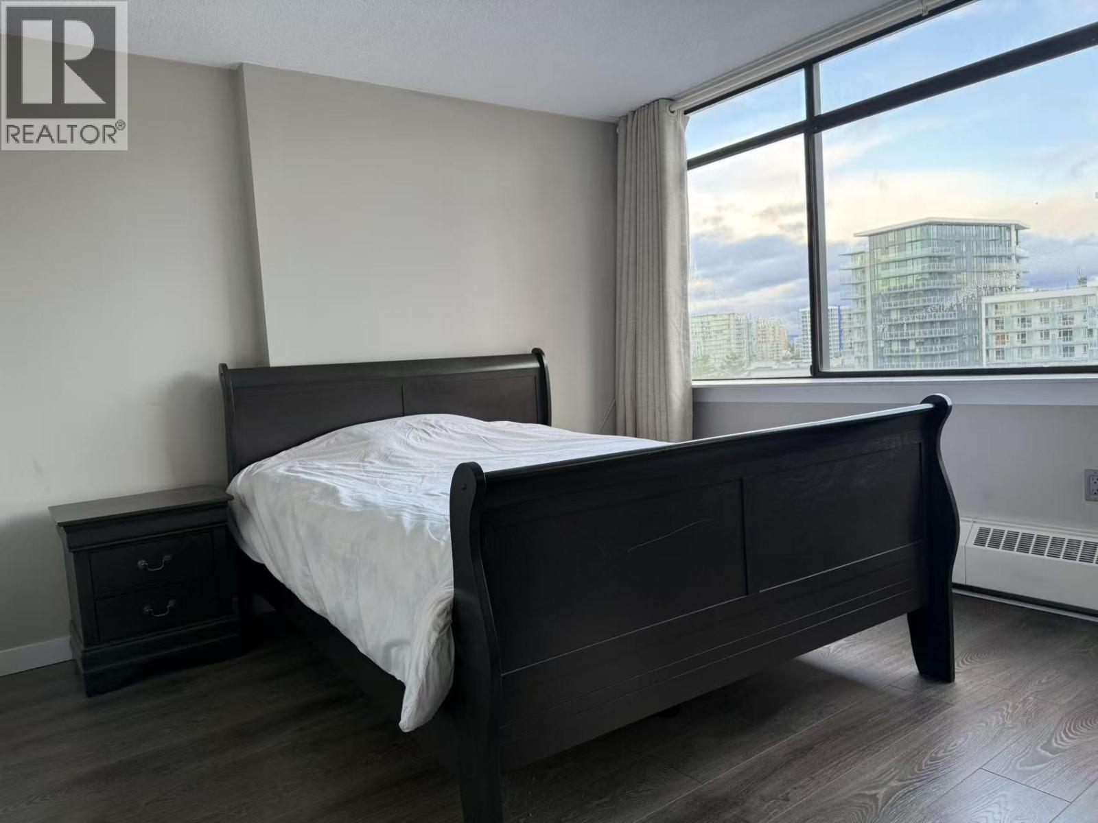 A bedroom with a large bed and a window overlooking a cityscape.