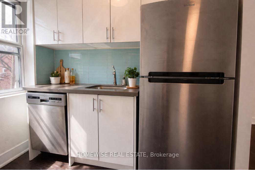 A stainless steel refrigerator stands in a kitchen with white cabinets and a dishwasher.