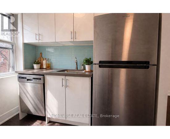 A stainless steel refrigerator stands in a kitchen with white cabinets and a dishwasher.