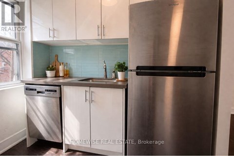 A stainless steel refrigerator stands in a kitchen with white cabinets and a dishwasher.