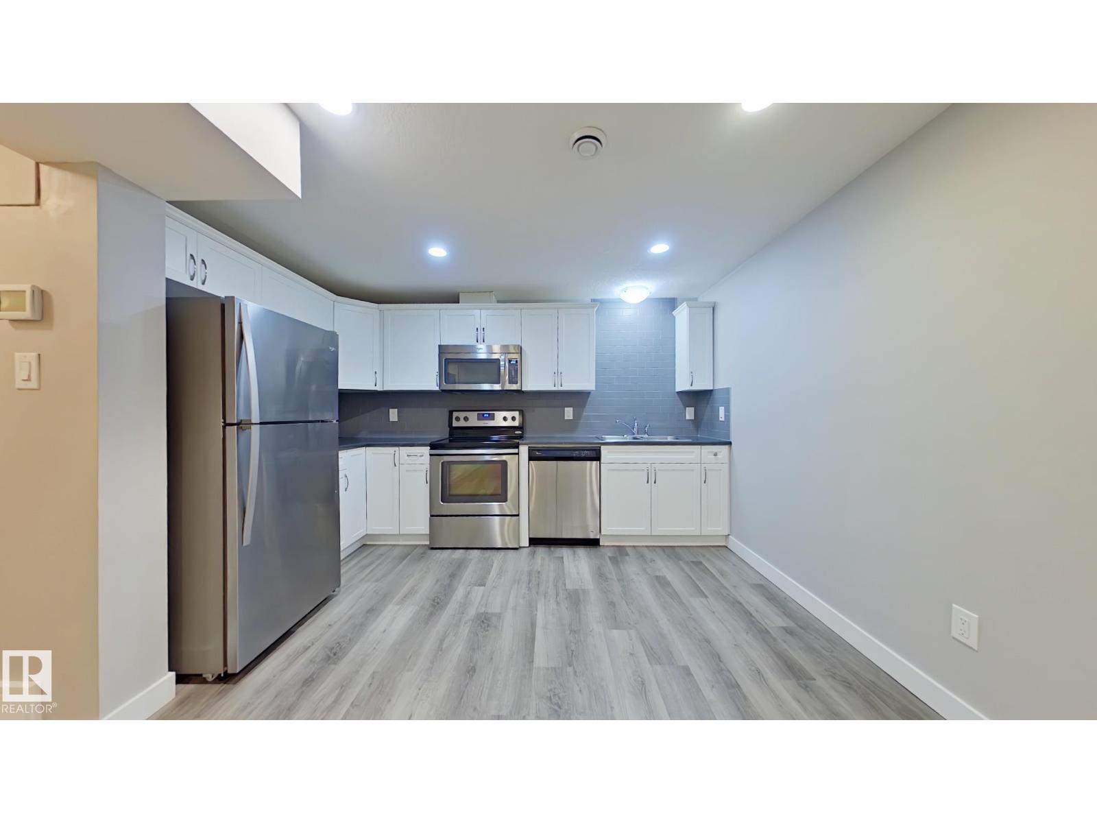 A kitchen with a refrigerator, microwave, oven, and sink.
