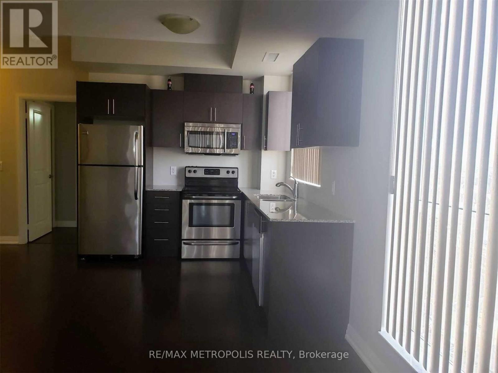 A kitchen with a refrigerator, microwave, oven, and sink.